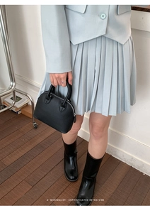 Minimalist black pebble leather shell bag paired with light blue suit and pleated skirt