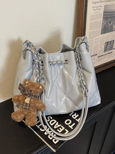 Grey quilted bucket bag with silver chain strap and brown teddy bear charm on black counter