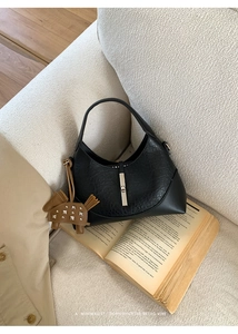 Chic black crescent handbag with silver buckle and horse charm on an open book