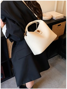 Detail view of cream white bucket bag with pebble leather texture and gold metal twist lock
