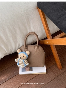 Brown lychee leather shell bag with round handles and a cute bear charm on a magazine