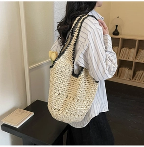 Detail of hand-woven straw tote bag with black trim and hollow texture on a wooden table
