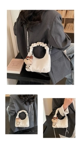 Detail of white pleated hobo bag with teddy bear charm and metal chain strap in daily setting