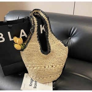 Detail of hand-woven straw tote bag with black contrast trim on a leather sofa