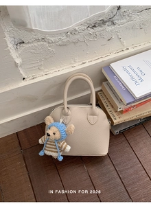 Detailed close-up of beige shell bag featuring a cute knitted bear charm and lychee grain texture