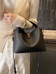 Elegant black lychee leather bucket bag with top handle and gold hardware in urban setting