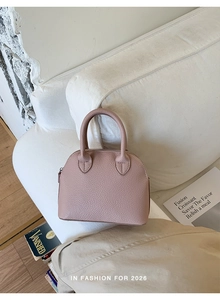 Detailed shot of pink shell handbag with litchi grain texture on a white sofa