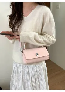 Close-up of a light pink leather crossbody bag with silver clasp on a white outfit