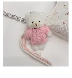 Nahaufnahme eines flauschigen Bärenanhängers mit rosa Strickpullover an Handtasche