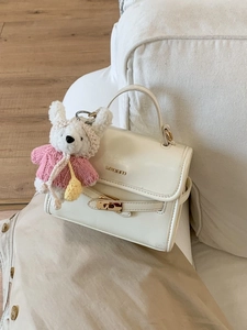 Fashionable cream white mini bucket bag with bear pendant on a soft white sofa