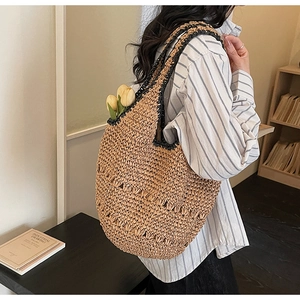 Close-up of a woven straw tote bag with hollow patterns and contrast black handles