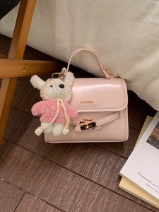 Pink fashion bucket crossbody bag with a cute bear plush toy charm on a soft background