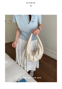 Detail of cream pleated tote bag showing the textured synthetic leather and drawstring knots
