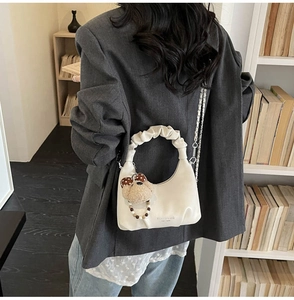 Detail of pleated handle and metal chain on a creamy crescent bag with a plush bear charm