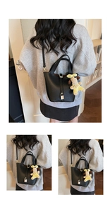 Detail of black pebbled leather bucket bag with silver padlock and plush puppy charm
