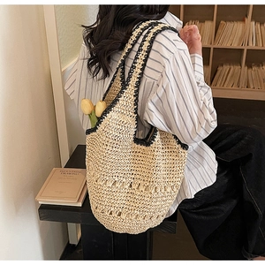 Detail of hand-woven straw tote bag with black contrast trim and hollow weave pattern