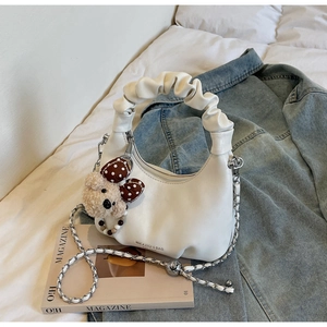 Close-up of white ruched hobo bag featuring a detachable plush bear charm and metal chain strap