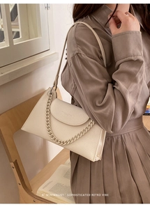 Detail of a minimalist off-white shoulder bag with matte chain on brown dress