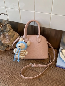 Pink lychee grain leather shell handbag with cute teddy bear charm on wood table