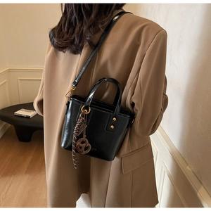 Detail view of a vintage black bucket bag with gold hardware and a woven charm