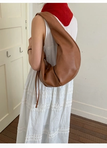 Detailed view of brown slouchy pleated crossbody bag worn by a model in soft interior
