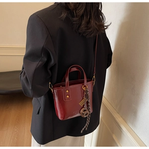 Model wearing dark red glossy bucket bag with metal charm and braided knot detail