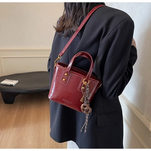 Detail of burgundy leather mini bucket bag with gold rivets and vintage twisted charm