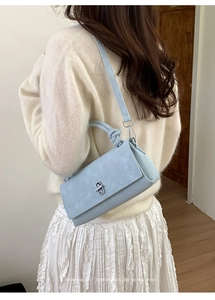 Light blue crossbody bag featuring a twisted handle and silver twist-lock on a beige outfit