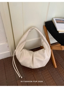 Detail of creamy white pleated croissant bag on wooden floor with minimalist aesthetic