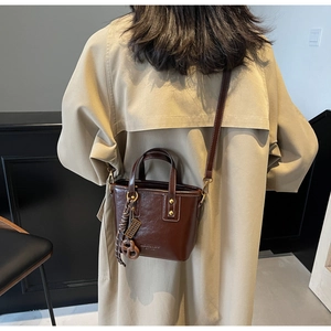 Detail of dark brown glossy leather mini bucket bag worn with a beige trench coat