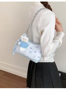 Detail der hellblauen Umhängetasche mit Cartoon-Print und Plüschbär-Anhänger am Modell