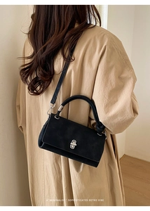 Minimalist black matte suede baguette bag shown styled on a khaki trench coat