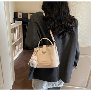 Détail du sac seau beige avec charme en peluche et logo de la marque sur un mannequin