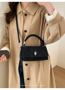 Close-up of a black minimalist leather crossbody bag with a silver metal twist lock detail
