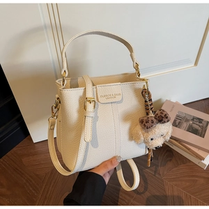 Detail of cream bucket bag in pebble leather with plush puppy charm and strap