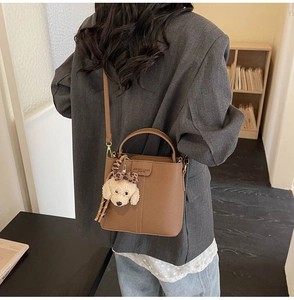Brown lychee leather bucket bag styled with a cute puppy charm and striped scarf detail