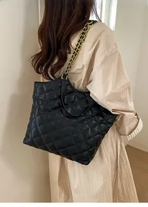 Detail of black quilted tote bag with gold chain strap worn by model for daily commute