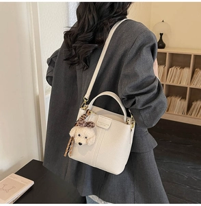 Detail of off-white lychee texture bucket bag with plush dog charm and leather embossing