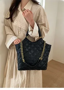 Detail of black quilted leather tote bag with elegant gold chain strap worn on beige coat