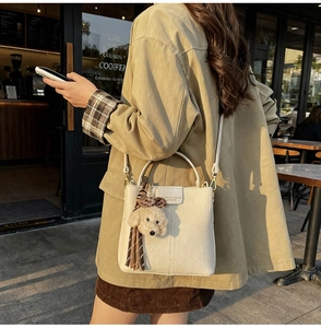 Detail of cream-colored textured bucket bag with teddy bear charm and fringe tassel