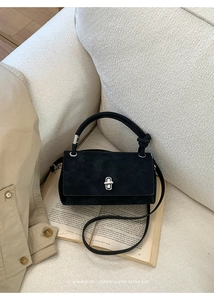 Close-up of black suede crossbody bag with knot handle and silver twist lock on sofa