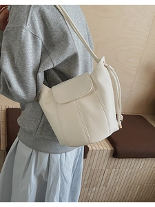 Detail view of cream bucket bag with lychee texture and side drawstring on model