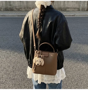 Brown leather bucket bag with a plush puppy charm shown on a street-style model