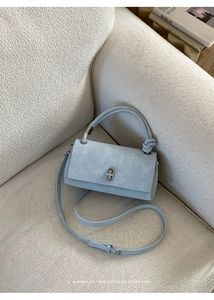 Close-up of light blue matte leather handbag with silver twist lock and knotted handle detail