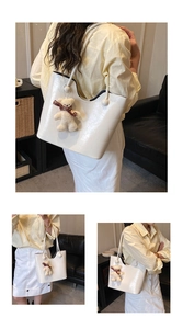 Close-up of white glossy tote bag with cracked leather texture and cute bear charm