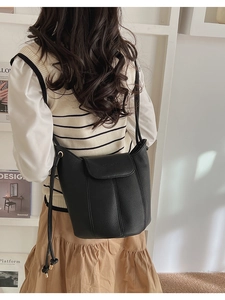 Detail of black lychee texture leather bucket bag worn as a crossbody with flap closure