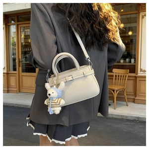 Beige lychee pattern crossbody bag with cute rabbit pendant shown on model in street view