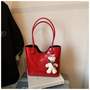 Macro shot of red patent leather tote bag with plush bear charm on a silver suitcase