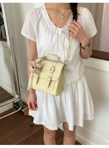 Detail of light yellow retro square bag with metal buckles and cute brown bear pendant