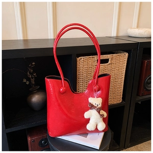 Detail of red glossy patent leather tote bag with cute bear charm and thin shoulder straps